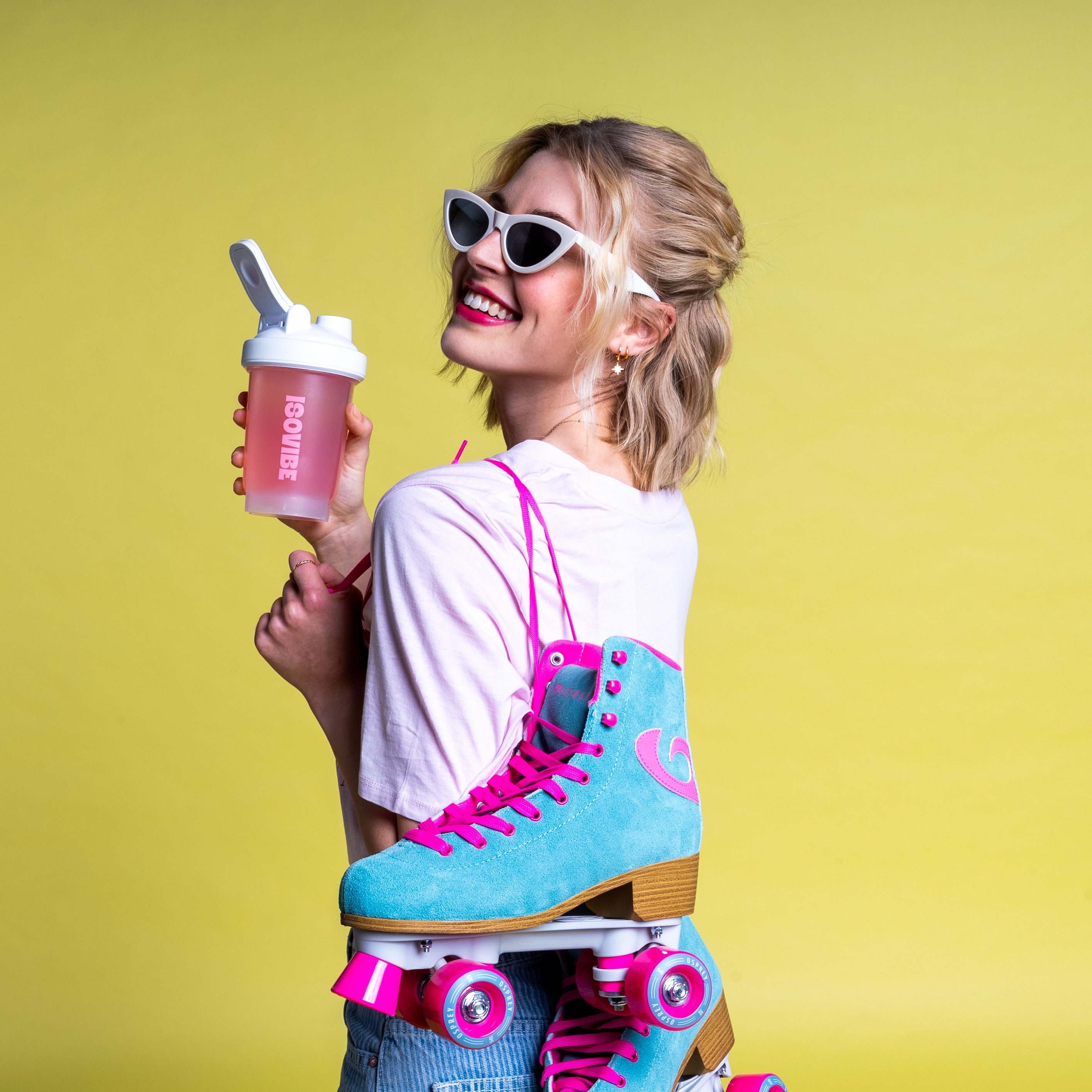 Girl smiling in light top with blue and pink rollerskates on shoulder and ISOVIBE shaker in hand