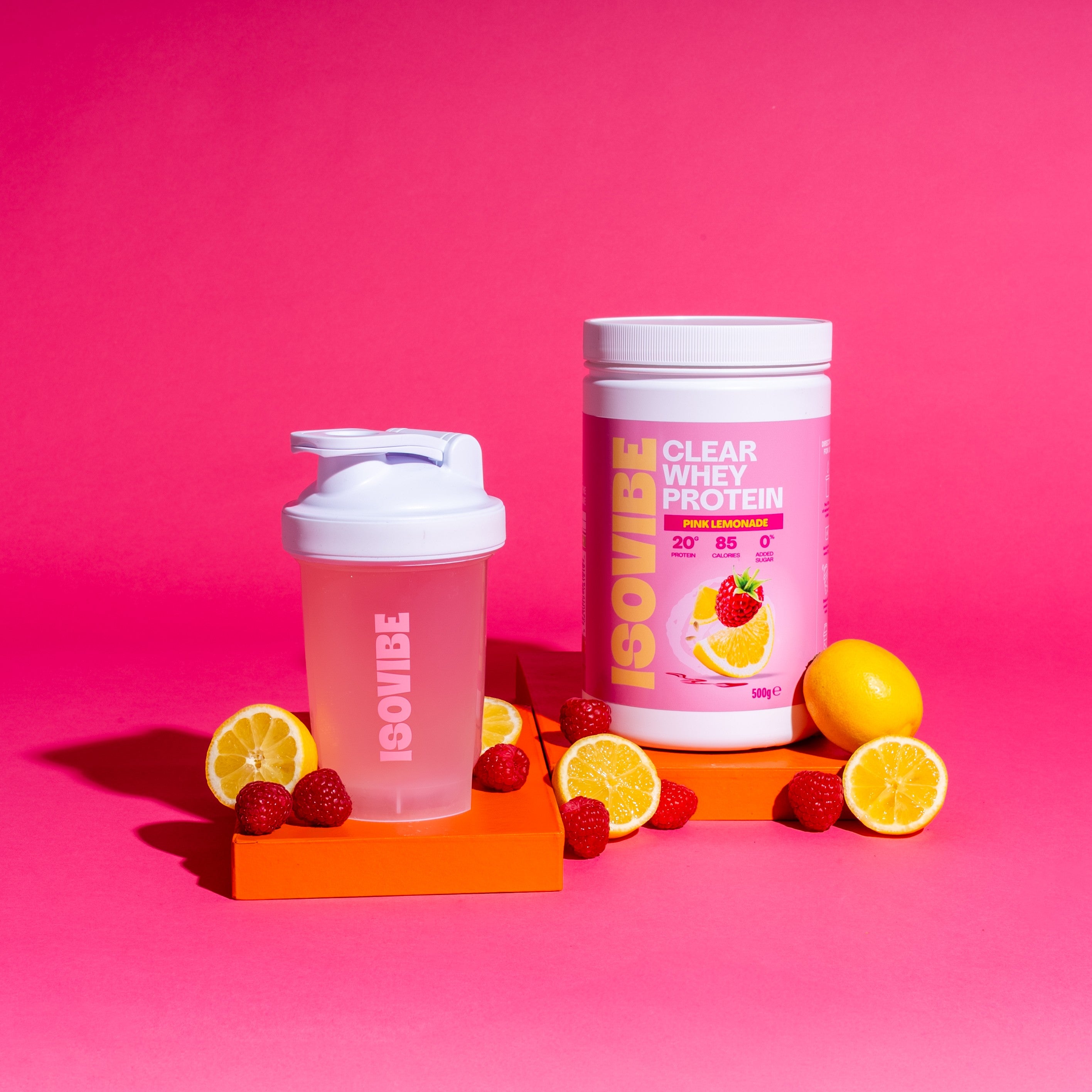 Pink Lemonade filled shaker and ISOVIBE tub on podiums with lemon and raspberries scattered in front