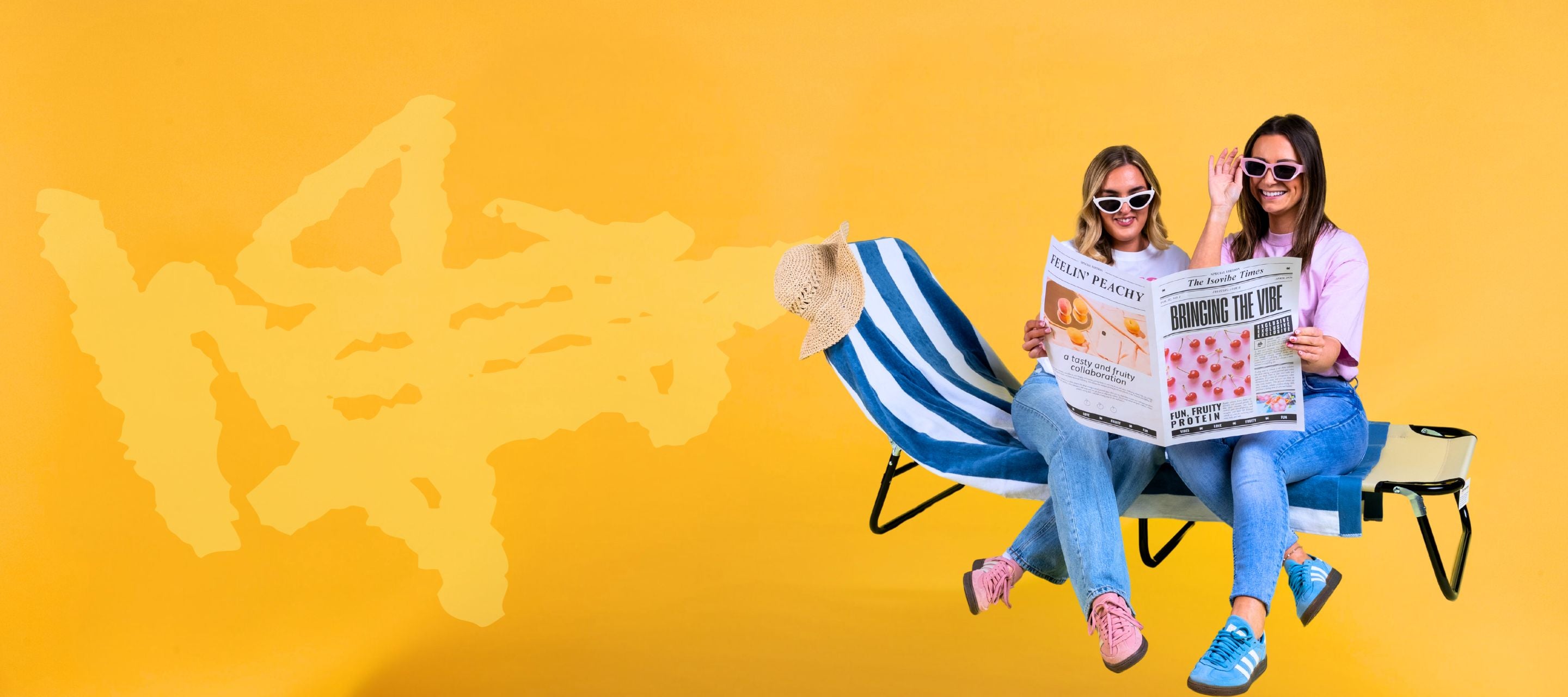 Two girls sat on sun lounger reading a newspaper with bright yellow background