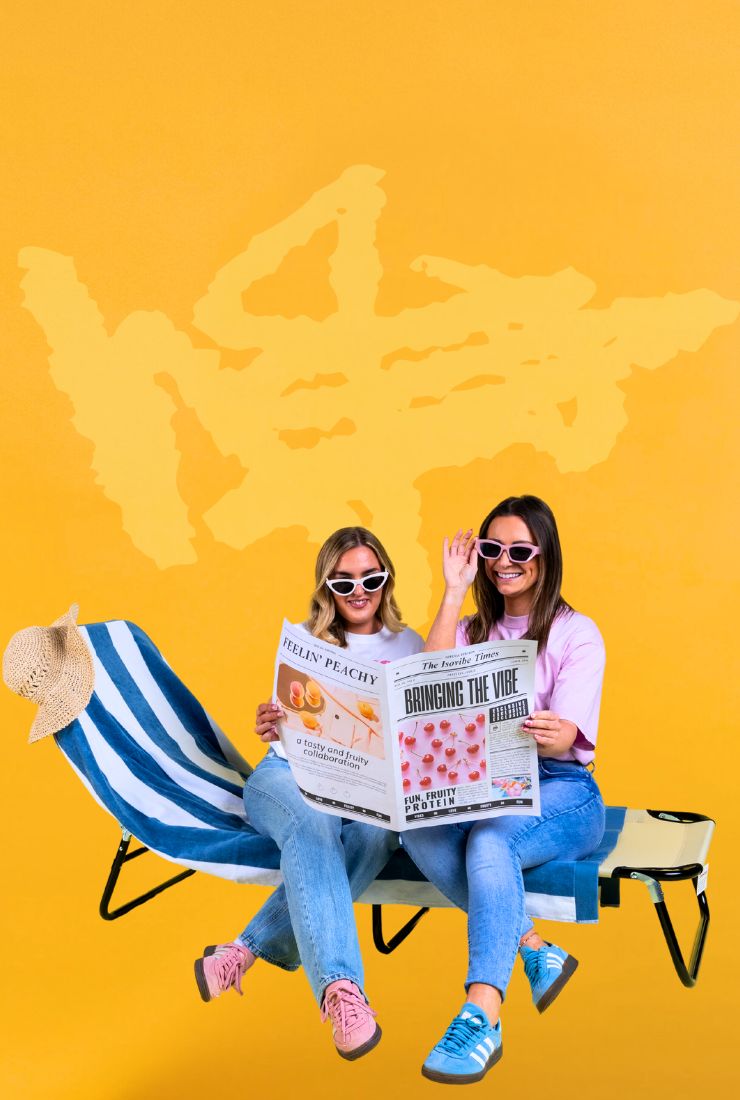 Two girls sat on sun lounger reading a newspaper with bright yellow background
