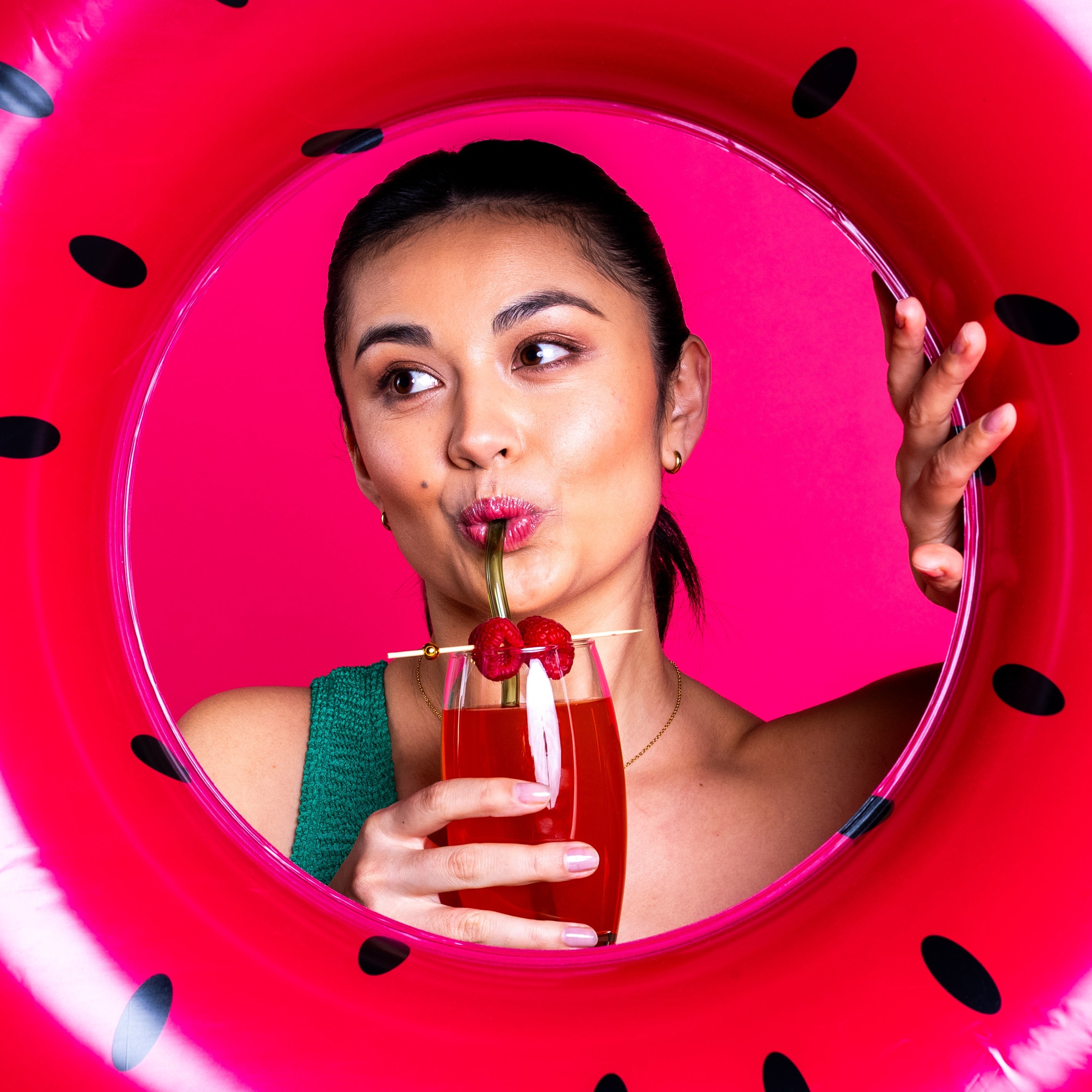 Girl sipping on her ISOVIBE peach and raspberry and peeping through a blow up inflatable ring that looks like a watermelon