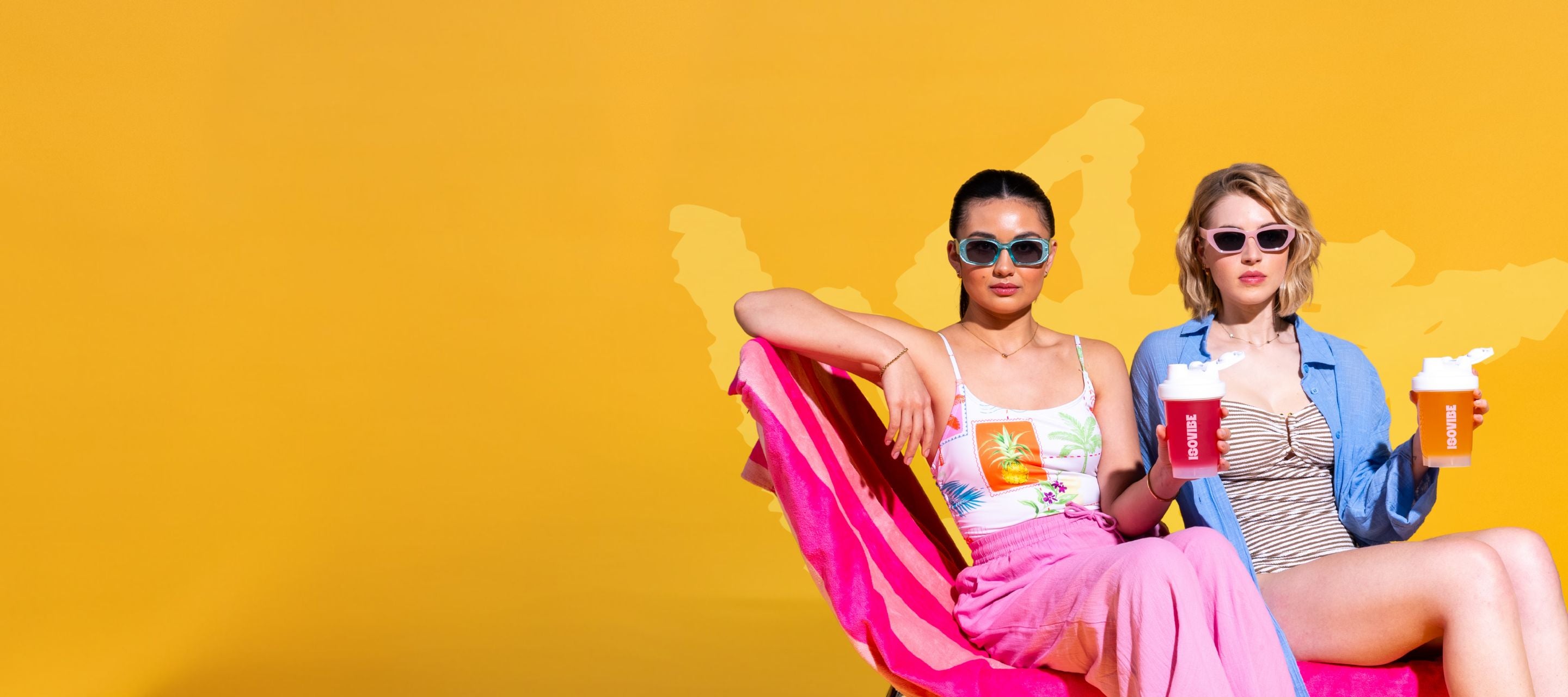 Two girls with sunglasses sat on a sun lounger holding drinks on a bright yellow background
